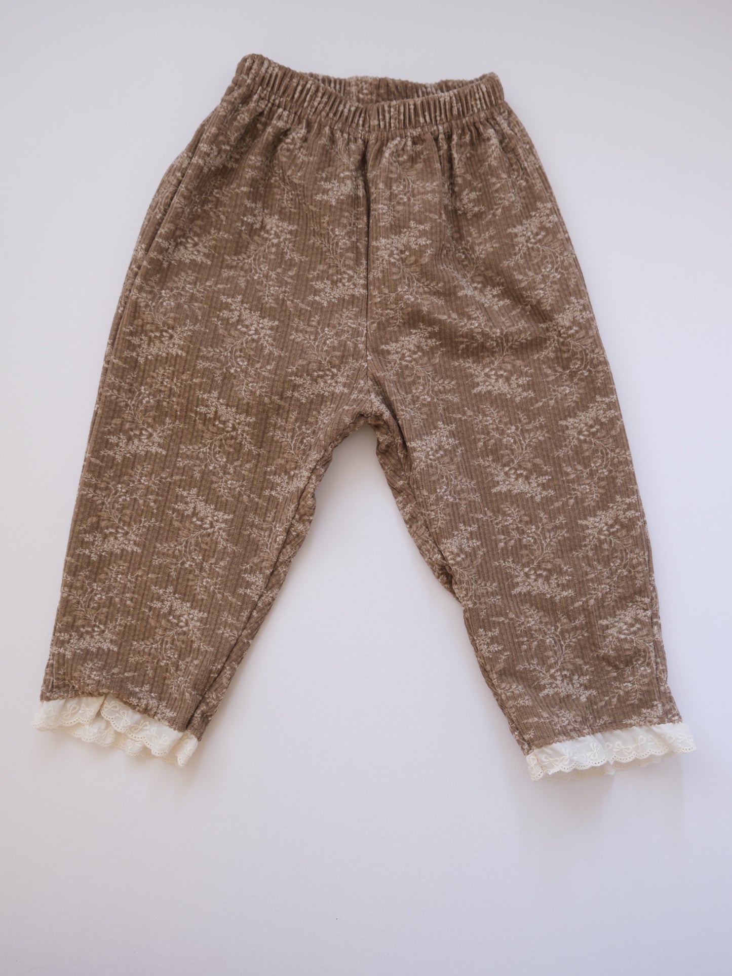 Brown patterned pants with lace trim on a white background
